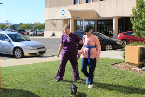 Inpatient Rehabilitation patient, along with Hutchinson Regional Medical Center staff member, walks outside the hospital with a dog.