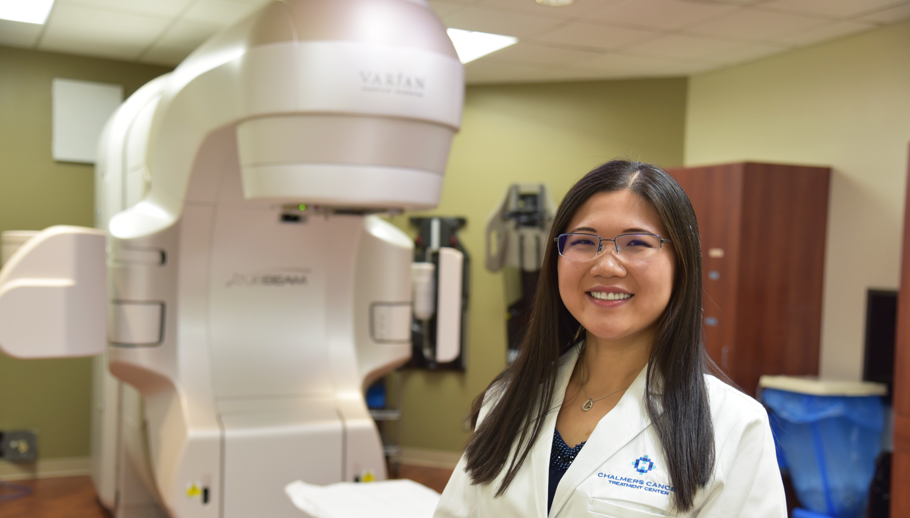 Dr. Shirley Butler-Xu, Radiation Oncologist, Hutchinson Regional Healthcare System, looking and smiling at camera with TrueBeam™ Linear Accelerator blurred out in background