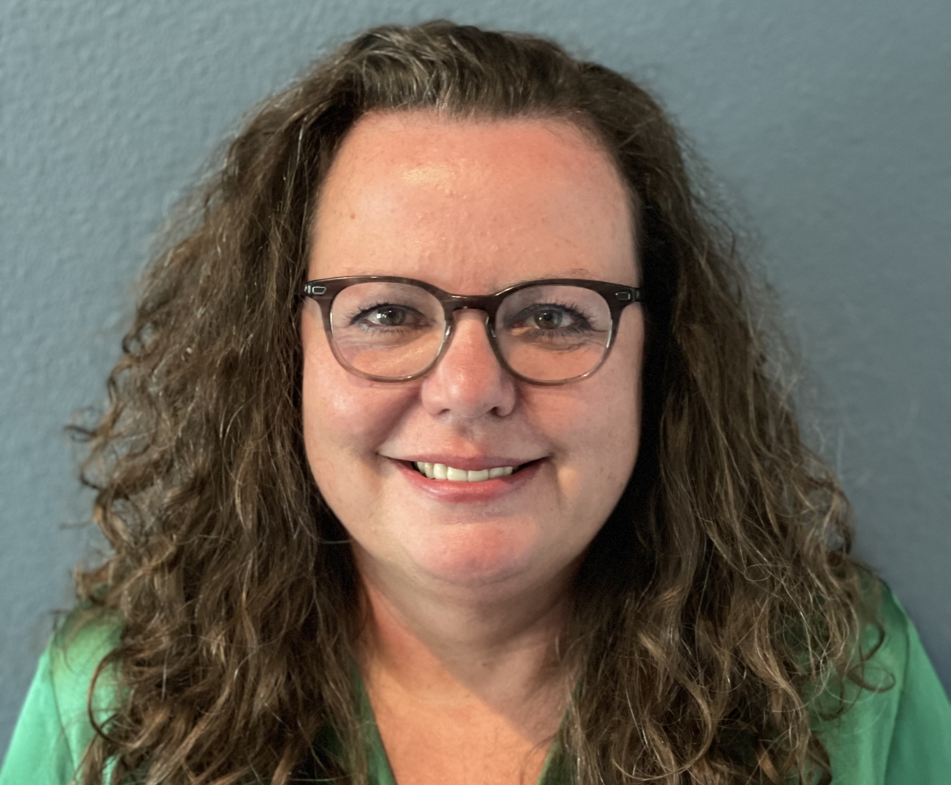 Dr. Jonna Jenkins, Chief Nursing Officer of Hutchinson Regional Medical Center, looking at the camera and smiling with a dark grey blue background.