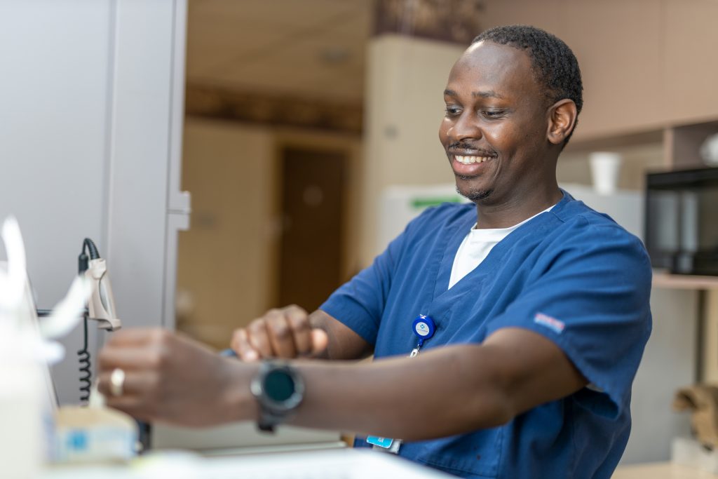 Male nurse in blue scrubs smiling.