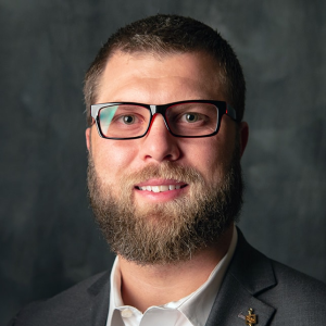 Dr. Nick Baldetti, Chief Quality Officer of Hutchinson Regional Healthcare System, wearing thick rimmed glasses, with a blurred out dark grey background.